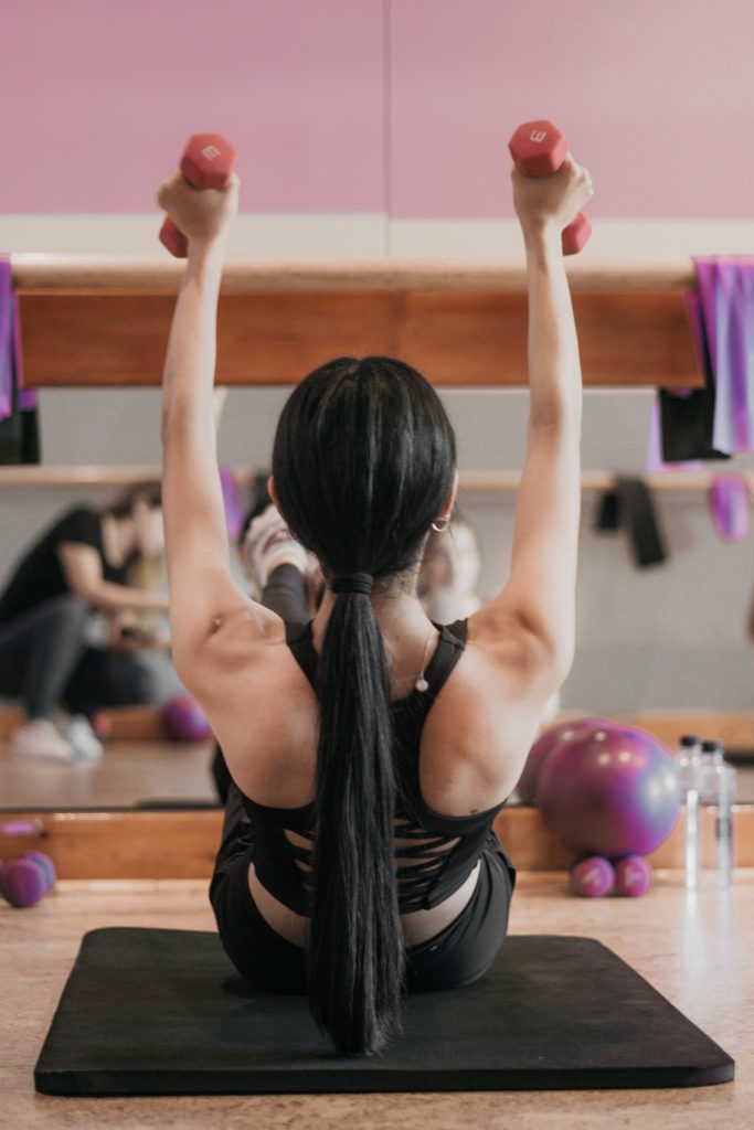 woman in in black tank top and black shorts sitting on yoga mat doing yoga streches