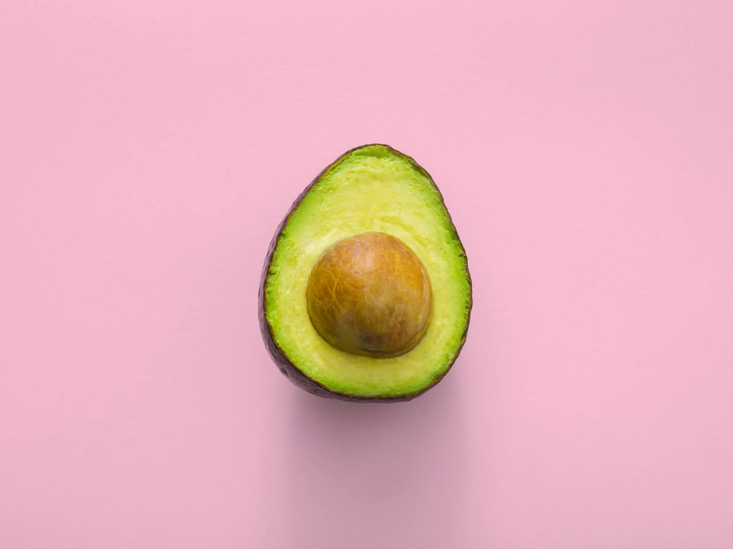 half avocado with seed shown with pink background ketosis food